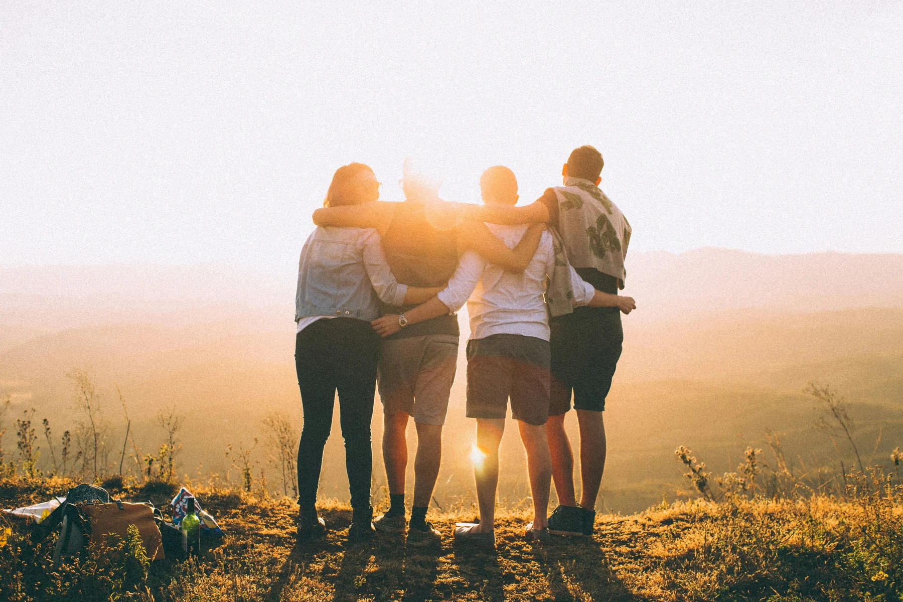 Four friends standing arm in arm at sunset